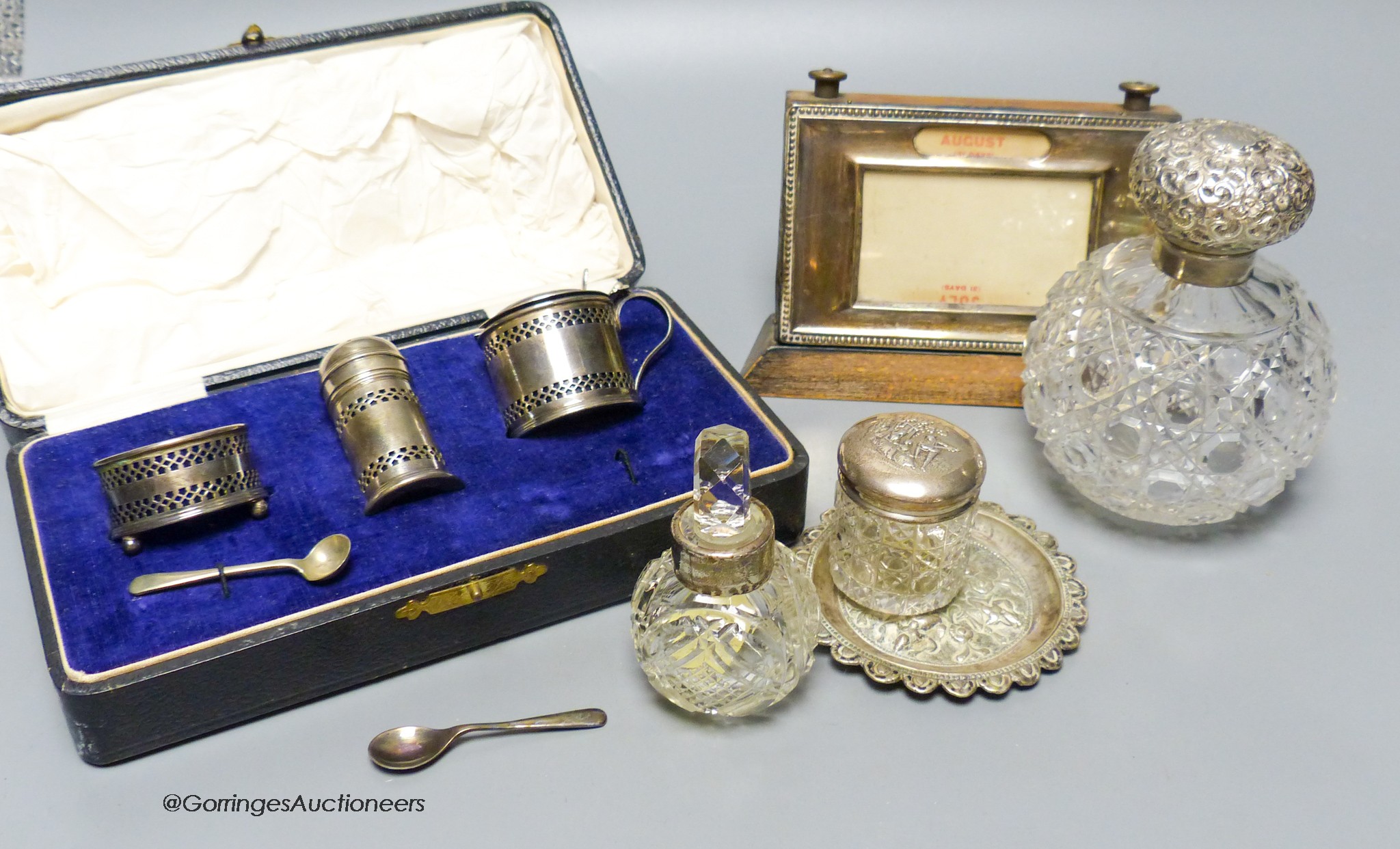 A cased silver condiment set, a silver mounted desk calendar, three mounted glass toilet jars and a Thai white metal small dish.